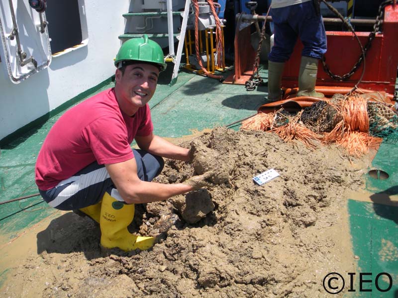 Curro López sobre el material recogido por la draga de arrastre bentónica, sostiene sobre sus manos una chimenea carbonatada autigénica, producto de la actividad bacteriana en el consumo de metano ©IEO