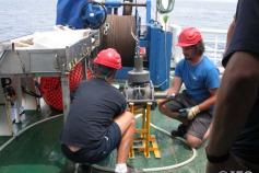 Manuel Piñeiro, “Manu”, de espaldas, corredor matutino de fondo, junto a Santiago Baluja, revisan la draga de cuchara Shipeck antes de disponerla para arriarla en la estación de muestreo ©IEO